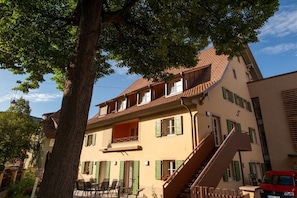 Ein zweistöckiges Gebäude mit Balkon, Treppe und Außenbestuhlung.