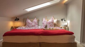 Une chambre avec un puits de lumière, un lit recouvert d’une couverture rouge et deux tables de chevet avec des lampes.
