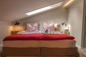 Una camera da letto con un velux, un letto con coperta rossa e due comodini con lampade.