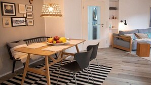 Un salon moderne avec un coin repas, comprenant une table en bois, des chaises noires, un tapis à motifs et un canapé avec des coussins.