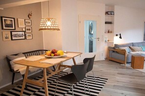 Un soggiorno moderno con zona pranzo, con un tavolo in legno, sedie nere, un tappeto decorato e un divano con cuscini.