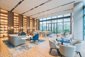 A modern hotel lobby with a large seating area, a coffee table, and a bookshelf. - Atour Hotel (Wuxi)