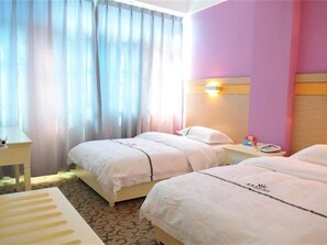 A hotel room with two beds, a bedside table with a lamp, and a window with curtains. - Yuhao Business Hotel (Dali)
