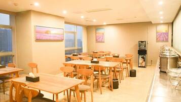 A hotel dining area with multiple tables and chairs, a buffet station, and artwork on the walls.