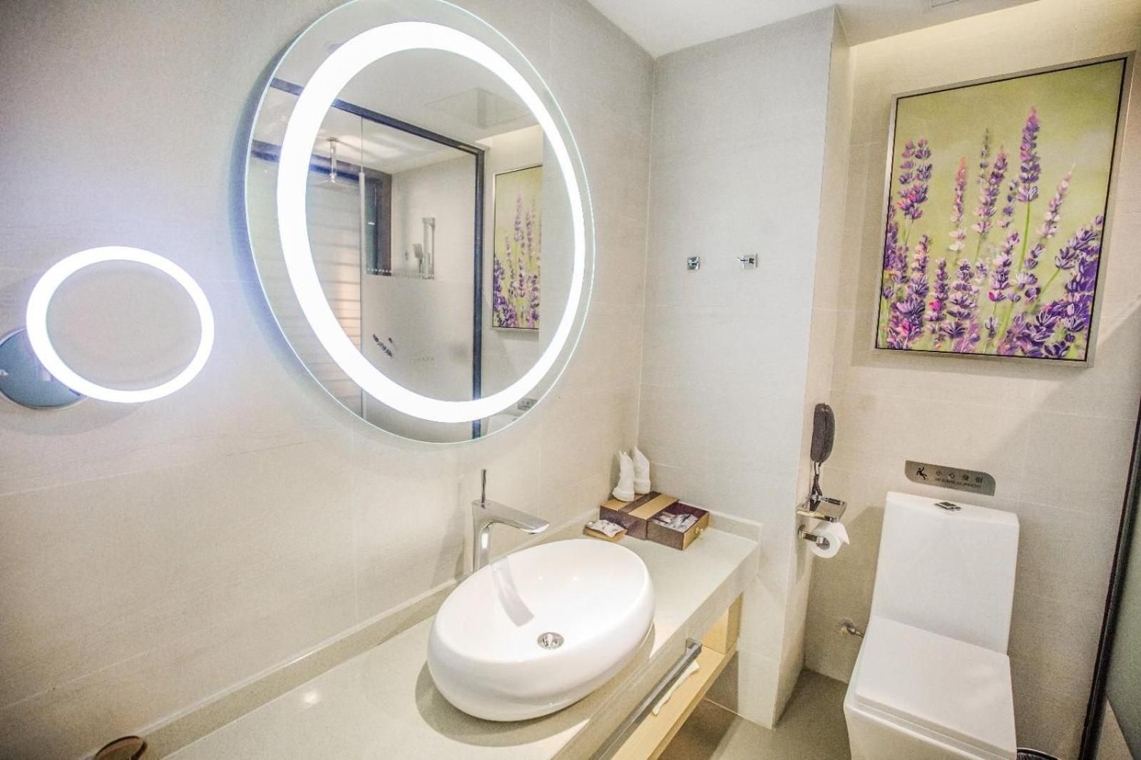 A modern bathroom with a round mirror, a white sink, and a toilet.