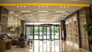 A hotel lobby with a revolving door, a reception desk, seating area, and a large window with a view of the parking area. - Greentree Inn Zhuma Railway Station Qian Plaza Branch (Zhumadian)