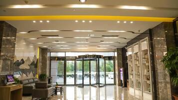 A hotel lobby with a revolving door, a reception desk, seating area, and a large window with a view of the parking area.
