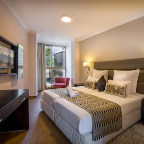 A hotel room with a bed, a TV, a desk, a chair, and a window with a view of greenery. - C Hotel (Mateh Yehuda)