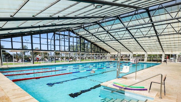 Una piscina interior con carriles delimitados, una estructura de techo y suelo de baldosas.