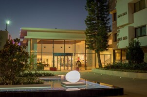 Entrada de hotel con fachada de vidrio, una recepción y una zona de piscina con una estructura esférica distintiva.