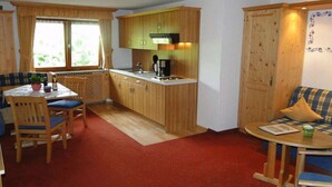 Een compacte keuken met houten kastjes, een eethoek met een tafel en stoelen, en een gezellig zitgedeelte met een bank en een bijzettafeltje.