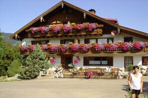 Um chalé tradicional com várias varandas decoradas com flores coloridas, cerca de madeira e céu claro.
