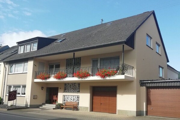 Een gebouw met twee verdiepingen, een balkon, een garage en een bank buiten.