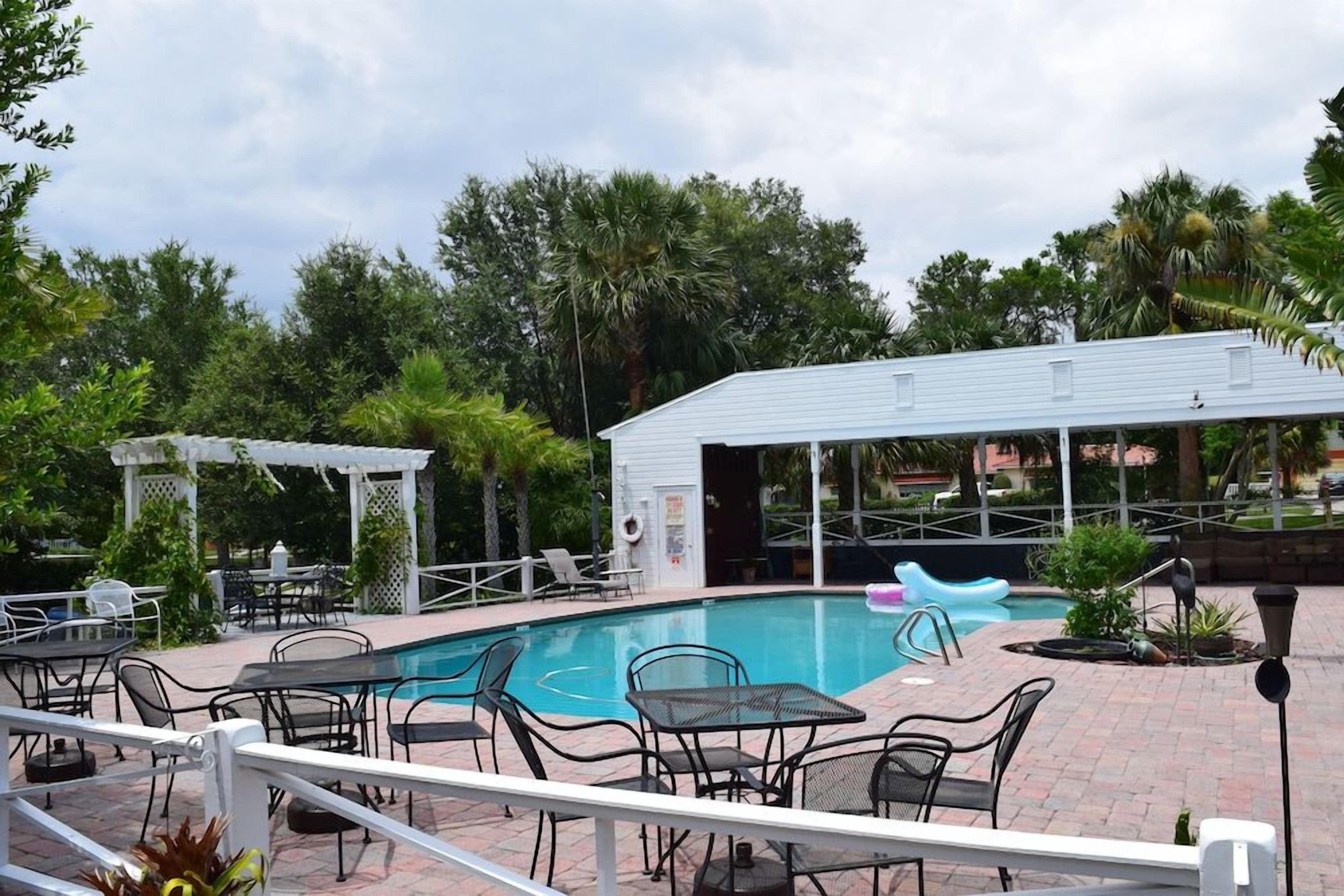 An outdoor swimming pool area with lounge chairs and tables, surrounded by greenery.