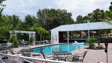 An outdoor swimming pool area with lounge chairs and tables, surrounded by greenery.
