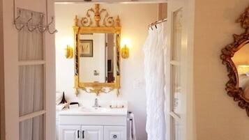 A bathroom with a white vanity, a large mirror with a gold frame, and a shower curtain.