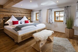 A wooden-framed bed with white bedding and red pillows, a white bench, and a potted plant. - Unterbrandnerlehen Apart Chalet Watzmann (Königssee)
