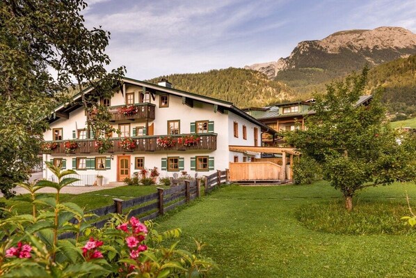 A traditional chalet with a balcony, surrounded by a well-maintained garden and a mountainous backdrop. - Unterbrandnerlehen Apart Chalet Watzmann (Königssee)