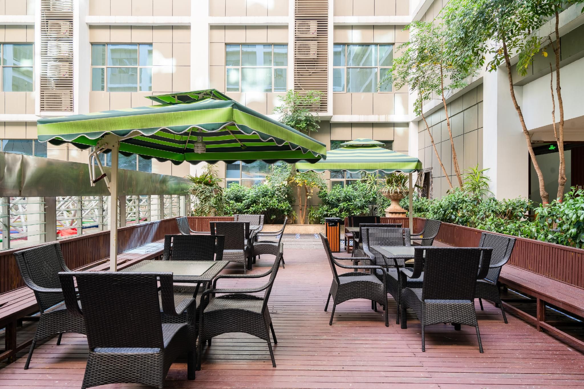 Un patio al aire libre con mobiliario de mimbre y sombrillas verdes a rayas.