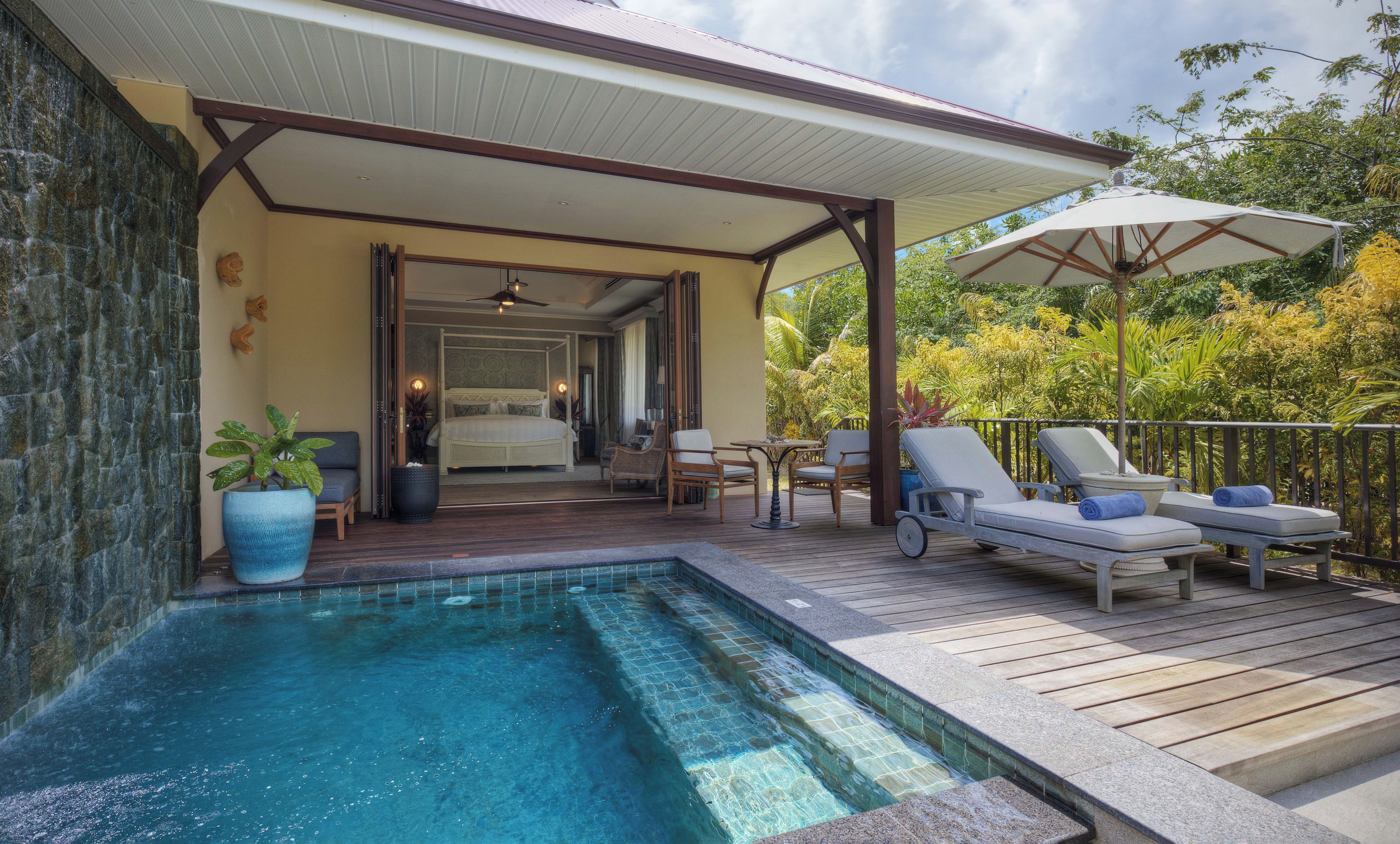 A pool area with a covered deck, lounge chairs, and a bedroom visible through an open door.