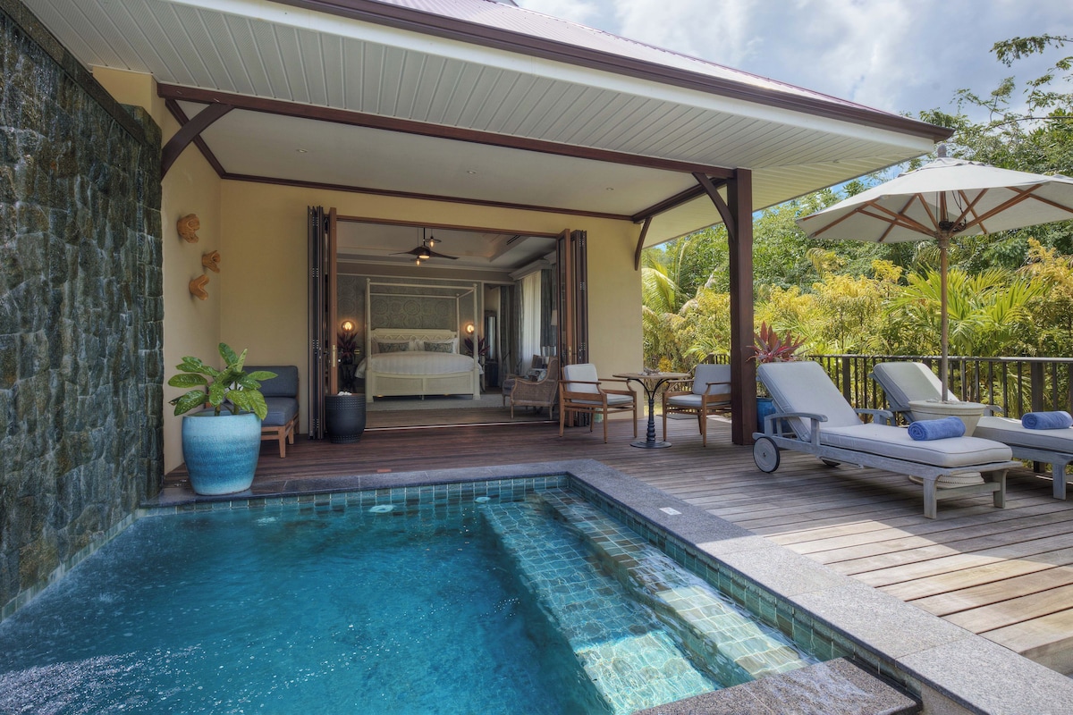 A pool area with a covered deck, lounge chairs, and a bedroom visible through an open door.