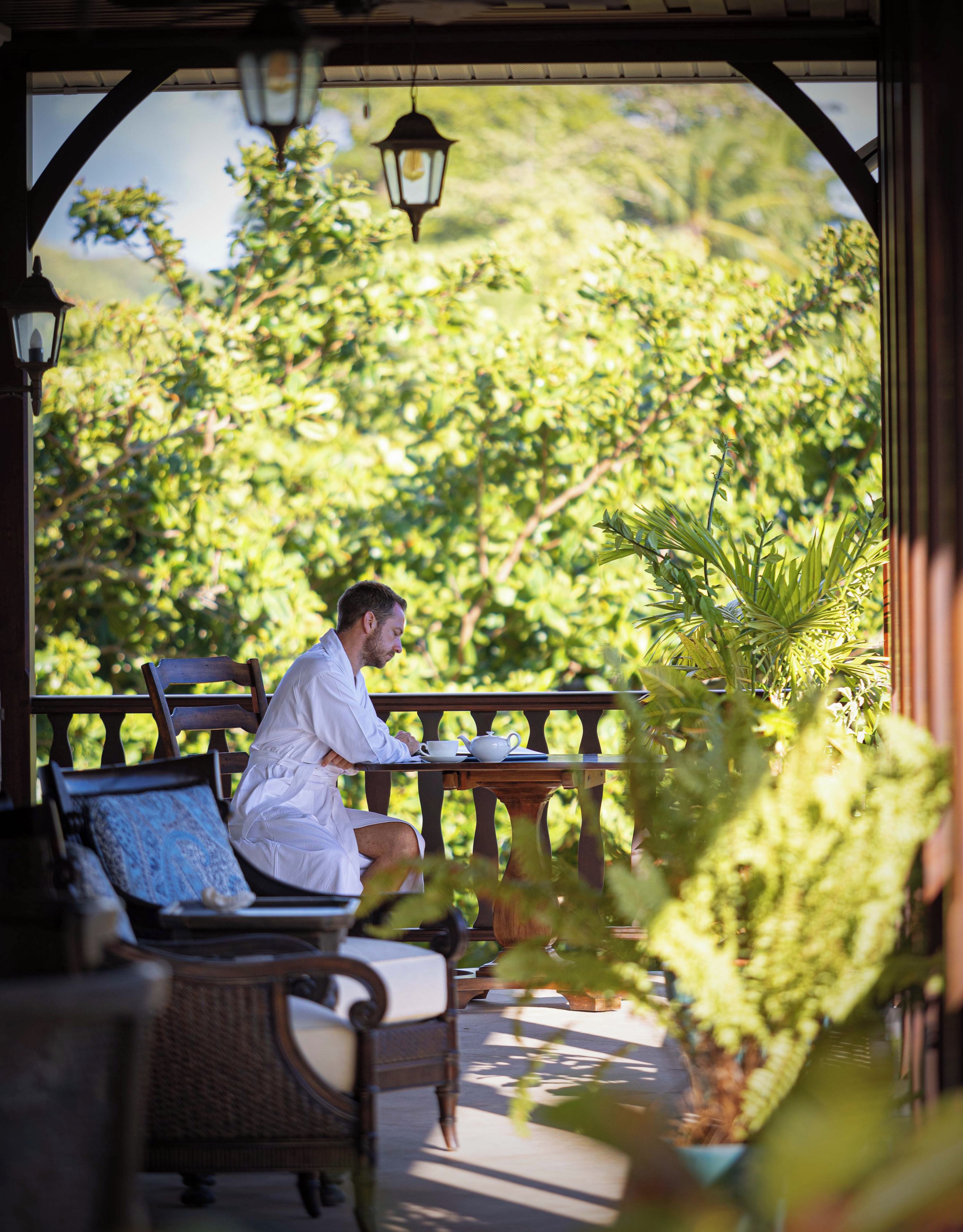 Una persona sentada a una mesa con vistas a vegetación exuberante y una estructura de pérgola.