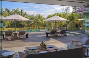 A poolside area with lounge chairs, umbrellas, and a view of a tropical garden.