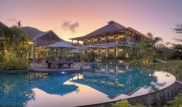 A resort with a swimming pool, lounge chairs, and a large building with multiple balconies. - La Cigale Estate (Anse Volbert Village)