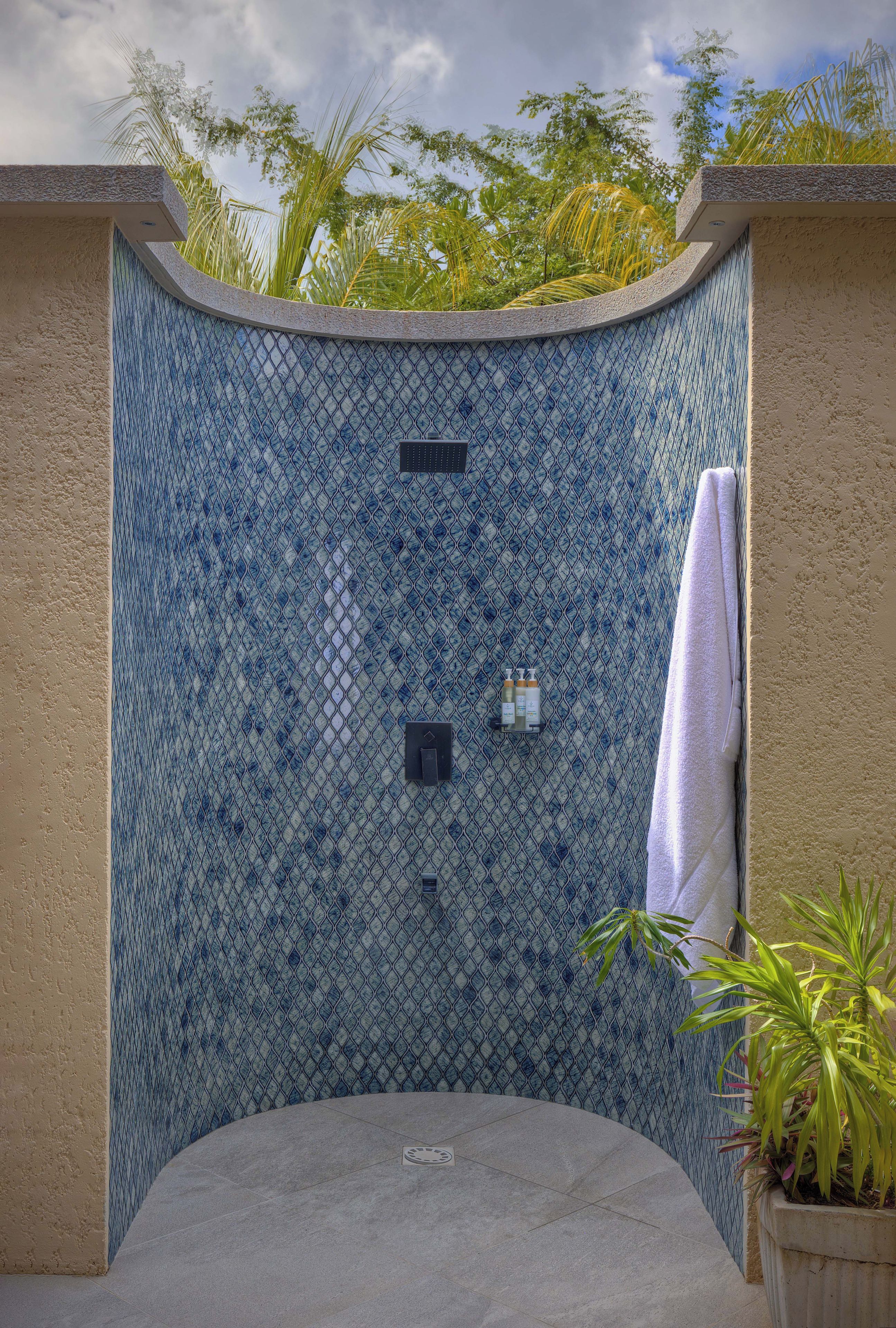 Un recinto de ducha con azulejos y diseño curvo, un perchero y una planta en maceta.