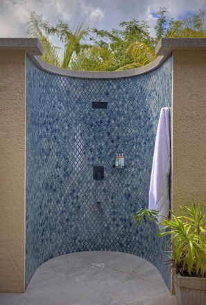 A tiled shower enclosure with a curved design, a towel rack, and a potted plant.