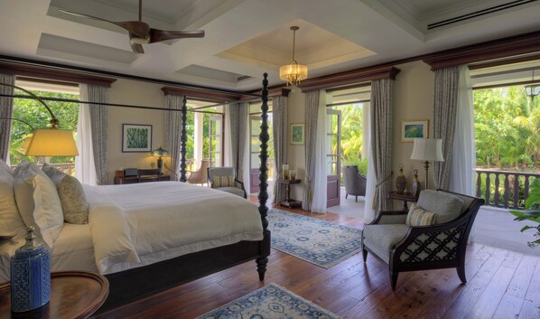 Une chambre spacieuse avec un grand lit, un coin salon avec un fauteuil et une vue sur une végétation luxuriante.