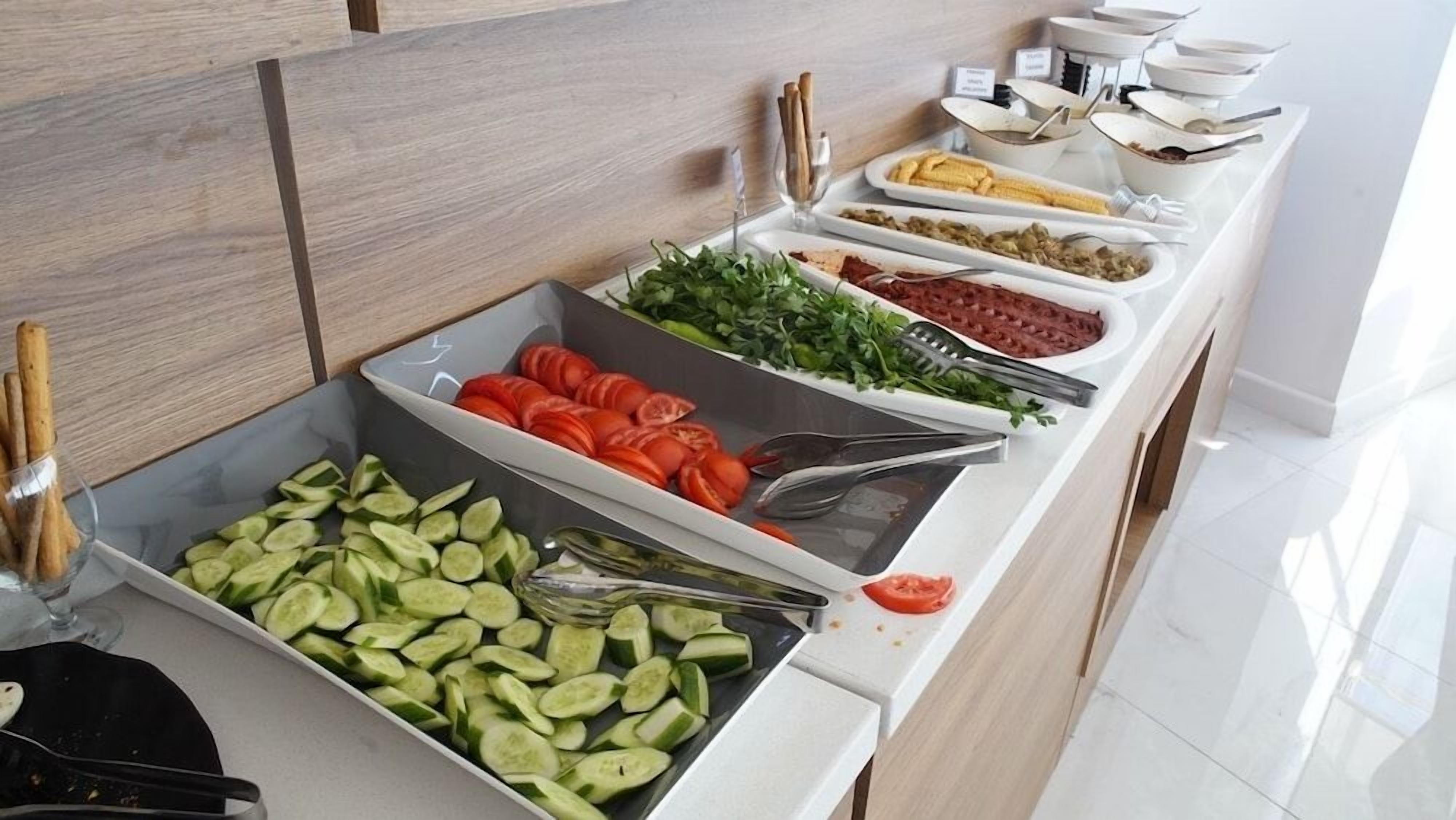 Ein reichhaltiges Buffet mit verschiedenen Speisen, darunter Gurkenscheiben, Tomaten, Salat und Fleisch.