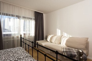 Une chambre à coucher avec un lit, un canapé, une fenêtre avec des rideaux et une vue sur l’extérieur.