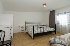 Un dormitorio con cama, una silla, escritorio y ventana con cortinas.