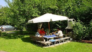 An outdoor dining area with a table and chairs under a white umbrella, surrounded by greenery. - Rolf Bauer on the 1st floor (Konstanz)