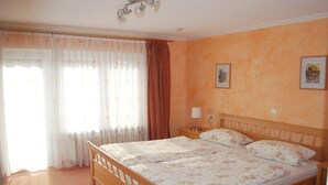 A double bed with a floral bedspread, a bedside table with a lamp, and a window with curtains. - Rolf Bauer on the 1st floor (Konstanz)