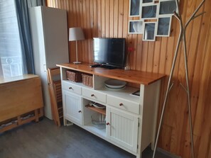 Ein gemütlicher Wohnraum mit einer Holzwand, einem Fernseher auf einer Holzablage, einer Lampe und einem Sessel.