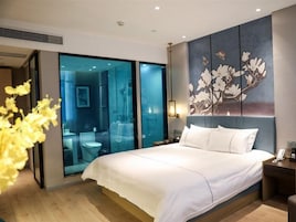 Quarto de hotel moderno com uma cama grande, divisória de vidro e uma obra de arte na parede.