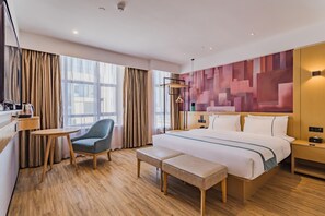 Habitación de hotel con una cama, una silla, una mesita, un banco y una pared con un diseño geométrico.