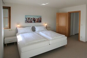 Quarto com cama de casal, mesas de cabeceira, criadeira e um quadro na parede, além de uma porta de madeira.
