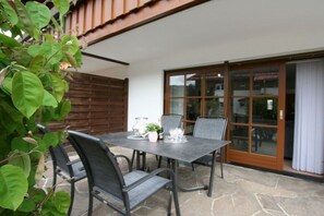 Pátio externo com mesa, cadeiras, cerca de madeira e porta de correr.