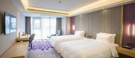 A hotel room with two beds, a desk, a chair, and a TV.
