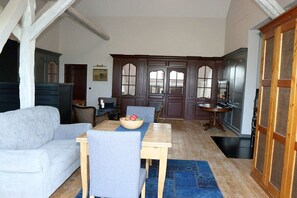 A dining area with a wooden table, blue chairs, and a bowl of fruit. There is a white sofa and a dark wooden cabinet in the background. - Erbschulzenhof (Müritz) (Buchholz (Müritz))