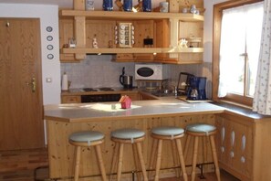 Una cocina con armarios de madera, un microondas, una cafetera y un ventanal con cortinas.