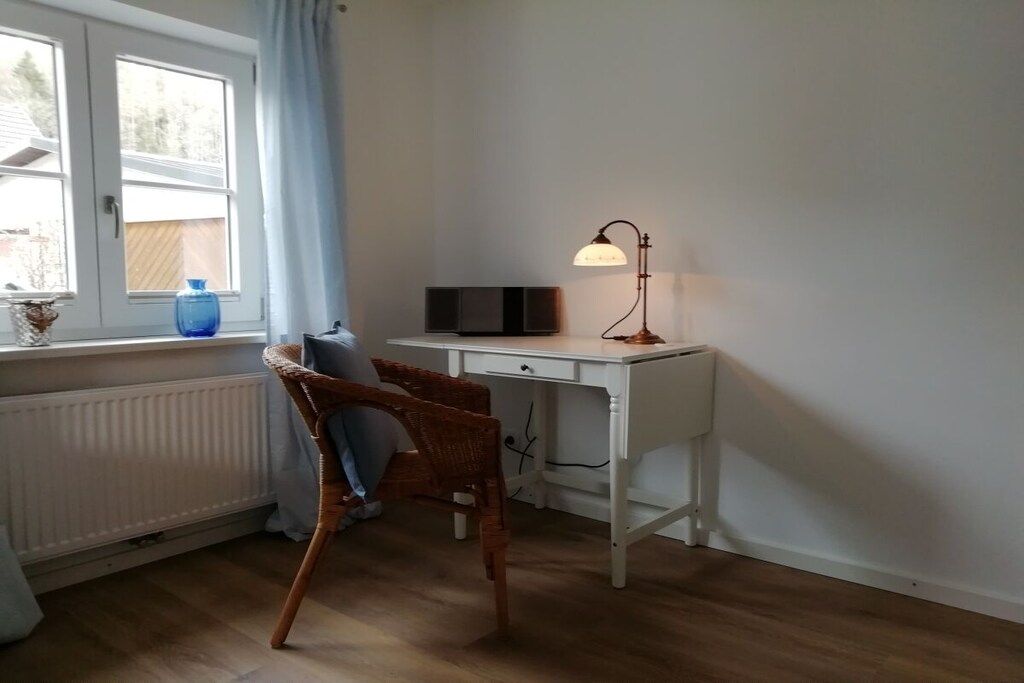 Une pièce avec un bureau blanc, une chaise, une lampe, un radiateur et une fenêtre avec des rideaux.