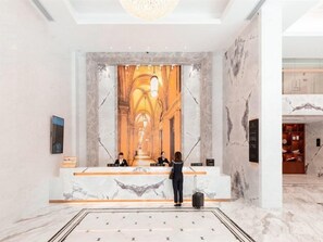 Zona de recepción de un hotel con paredes de mármol, un mostrador de recepción y un espejo grande y ornamentado.