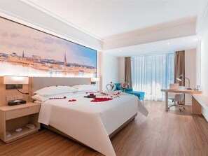 Habitación de hotel con una cama grande, un escritorio, una silla y vistas a un paisaje urbano.