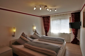 Quarto de hotel com duas camas, televisão e janela com cortinas.