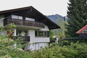 A two-story building with a balcony, surrounded by greenery and mountains in the background. - Alpenflair holiday apartment 213 "timeless" (Oberstdorf)