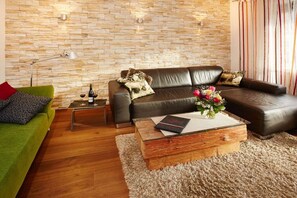 A modern living room with a stone wall, leather sofa, green couch, and a wooden coffee table with a vase of flowers. - Alpenflair holiday apartment 213 "timeless" (Oberstdorf)